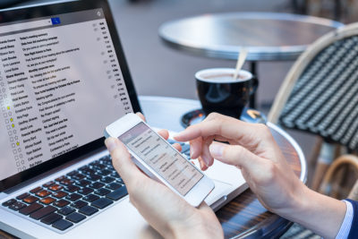 Business person reading emails on smartphone and laptop computer